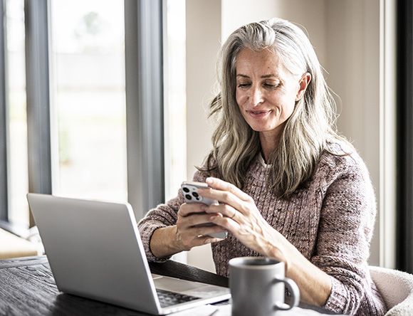 Person using smartphone at a table beside a laptop and coffee mug.Provide your feedback on BizChat