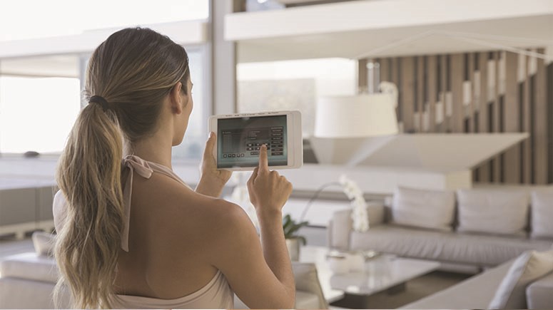 Young woman in summer top in a modern living room changing settings on a home control tablet 