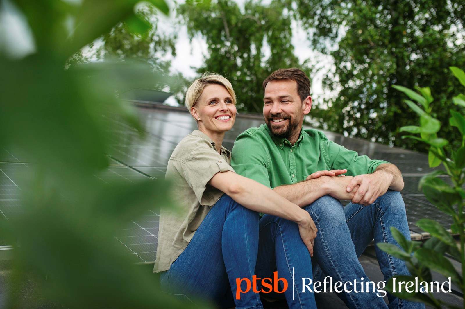 happy couple sitting on a roof filled with solar pannels