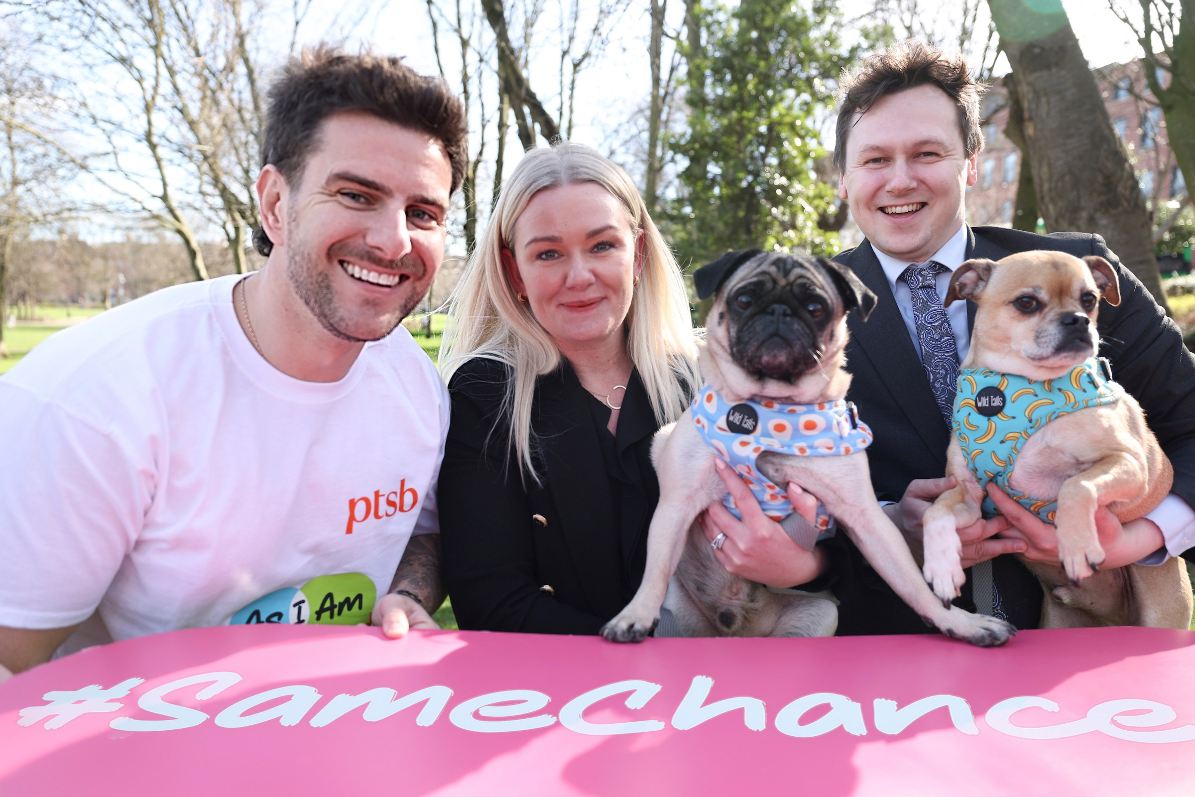 3 people, holding 2 small dogs and a banner with text #same chance