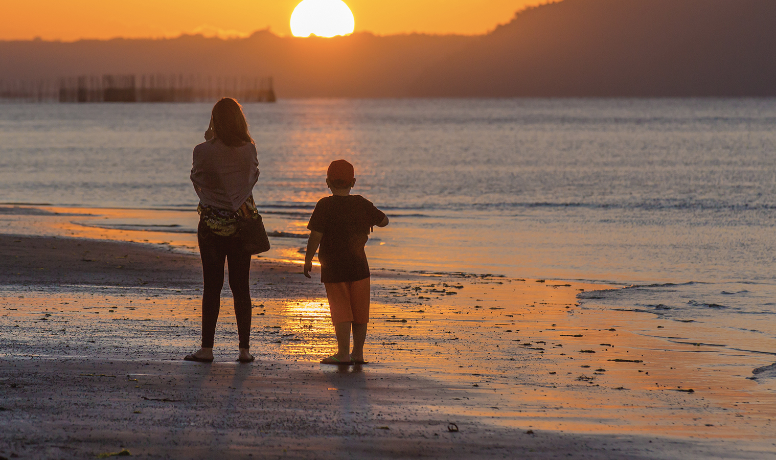 woman and a young boy at beach looking at a sunset
