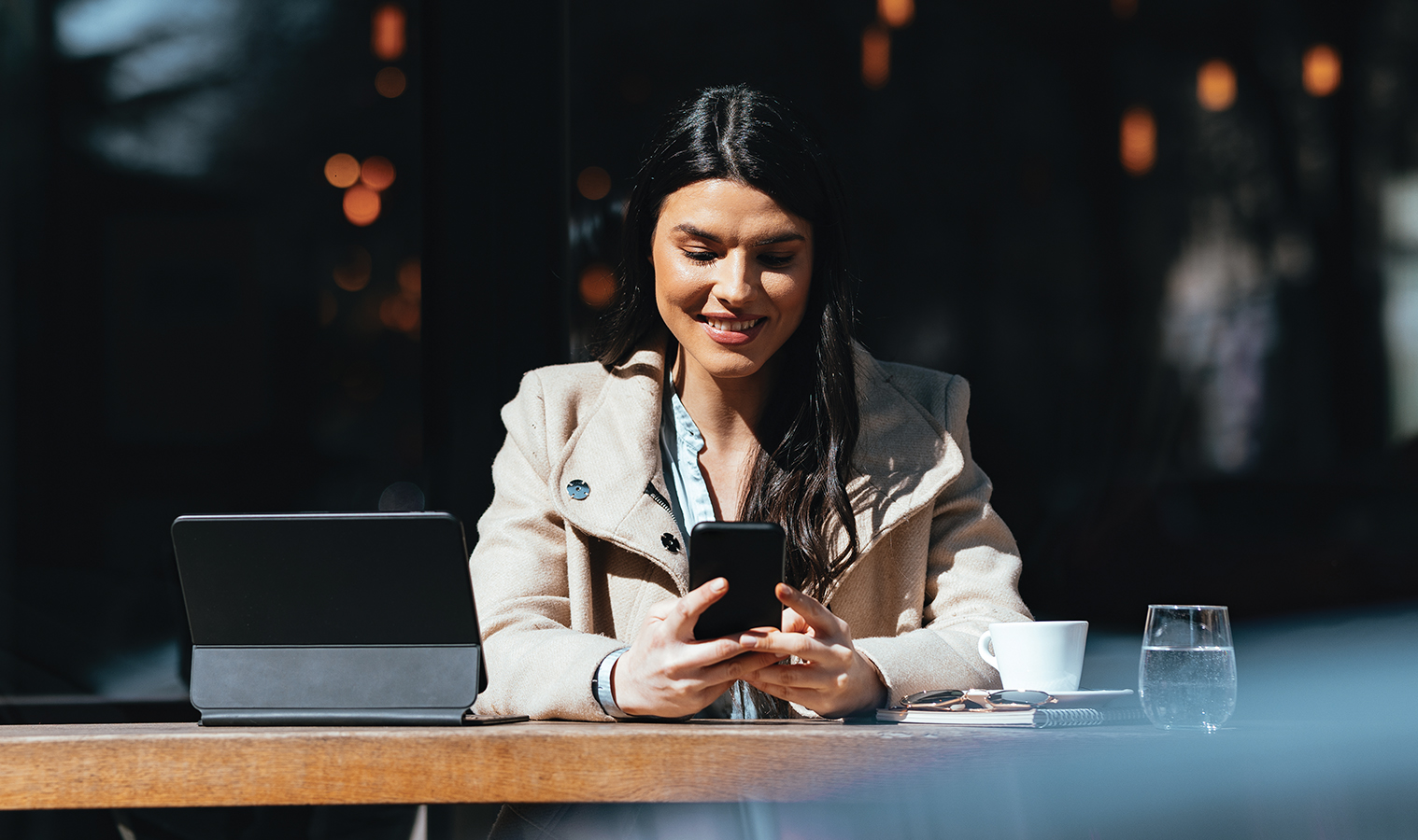 woman sitting in outdoor café browsing on her phone and laptop