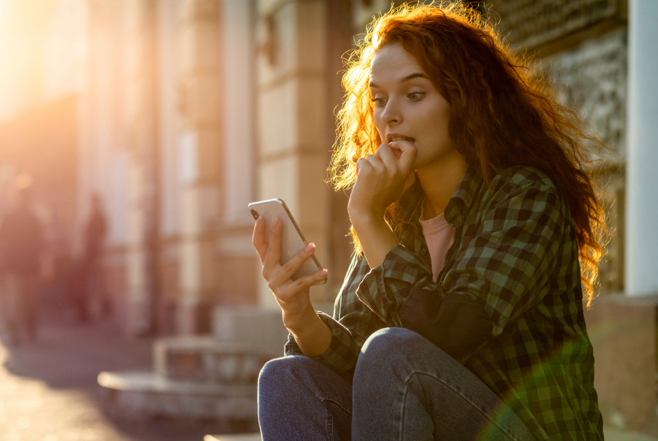 woman with long curly hair looking at her phone and biting her finger 