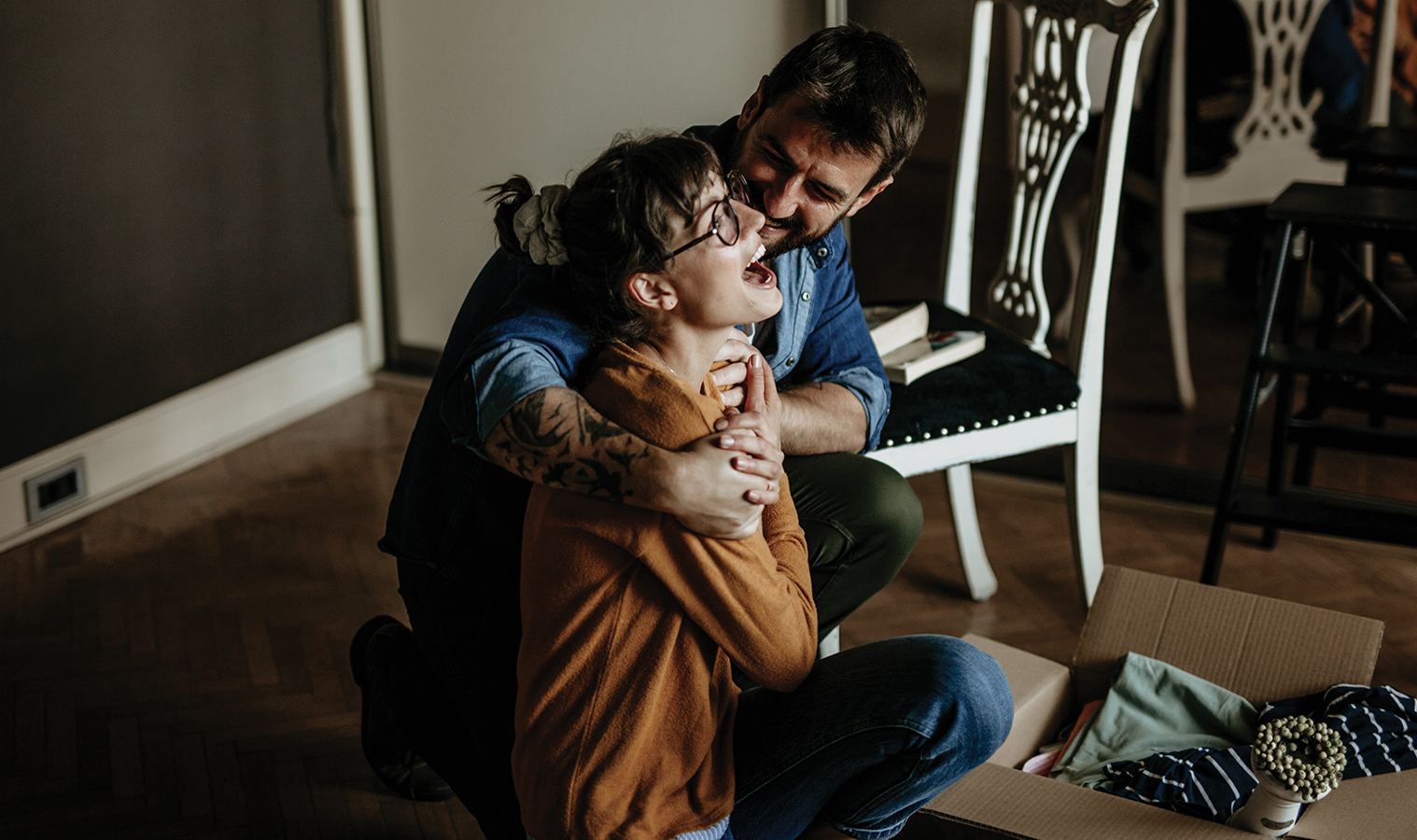 couple squatting on a floor and embracing while unpacking a box 