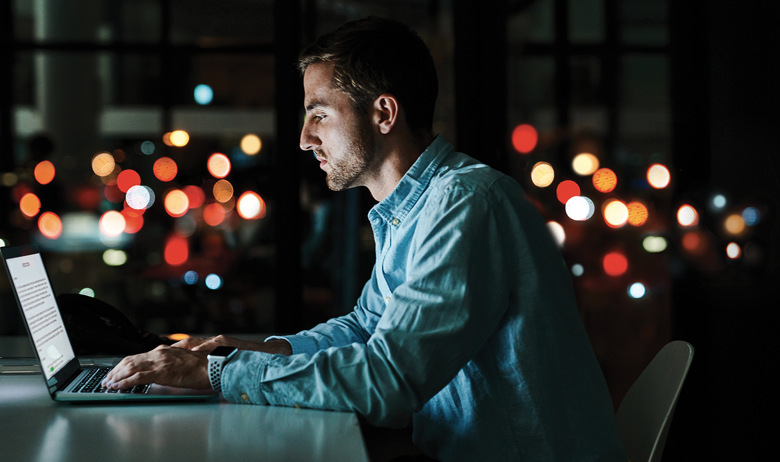 man sitting at a table working on his laptop, dark room with loads of small colorful lights in the background