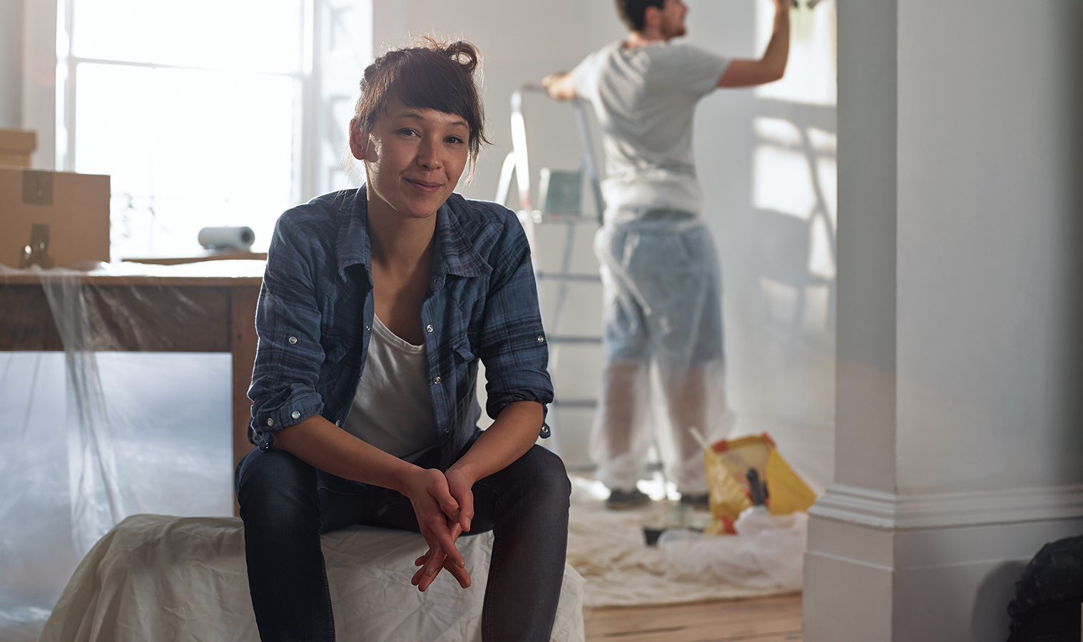 renovated room, man is paiting a wall in a background while a woman is sitting down and looking straight up, smiling 