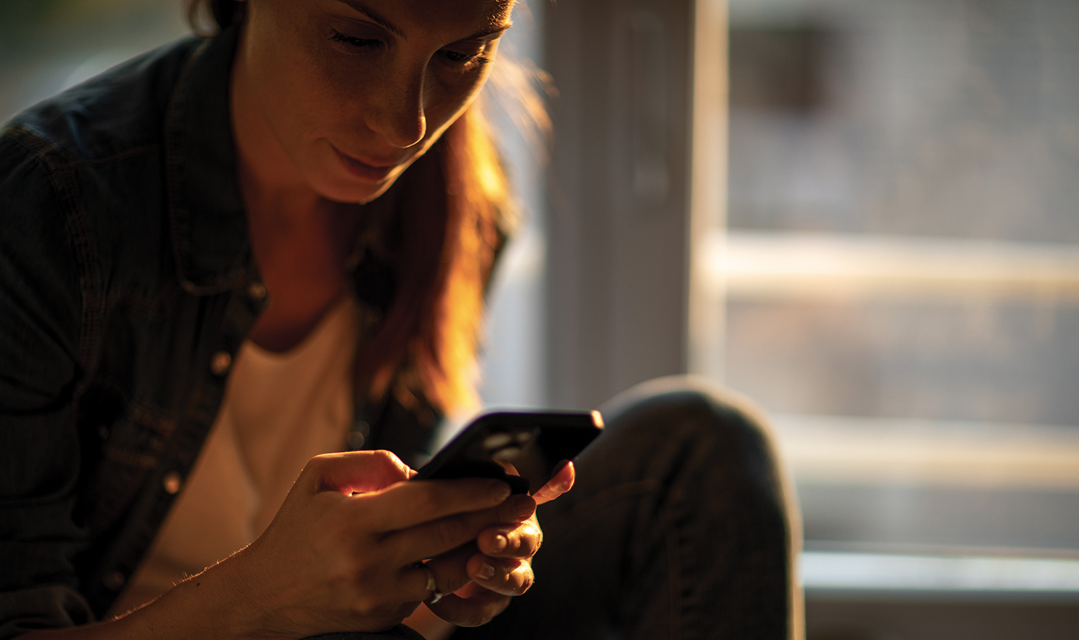 close up on a woman checking her mobile phone, soft sunset light in the background