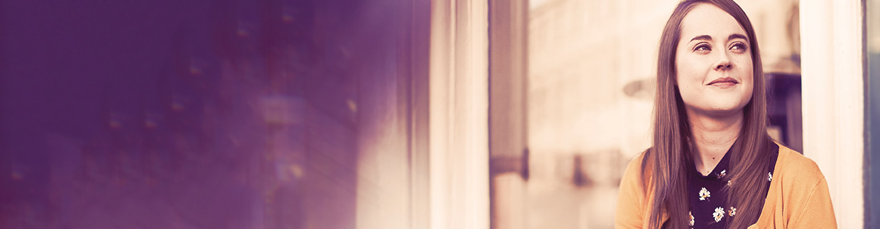 Close up on a woman smiling and looking up , standing in front of a big glass window