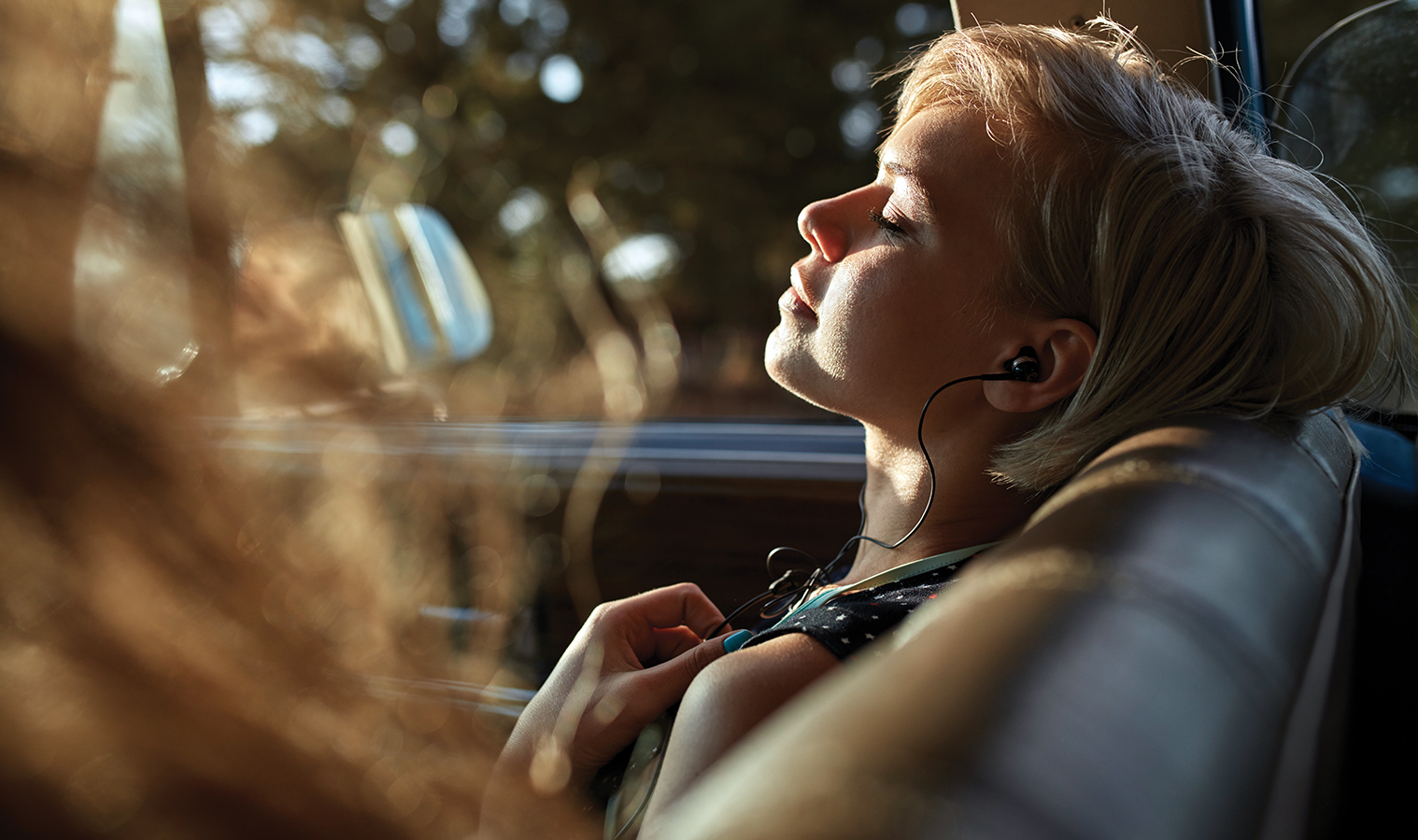 woman with short hair listening to music with her earphones while relaxing as a passenger in a car