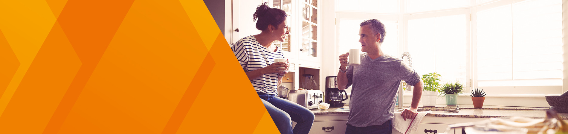 A couple at a kitchen counter talking and drinking coffee