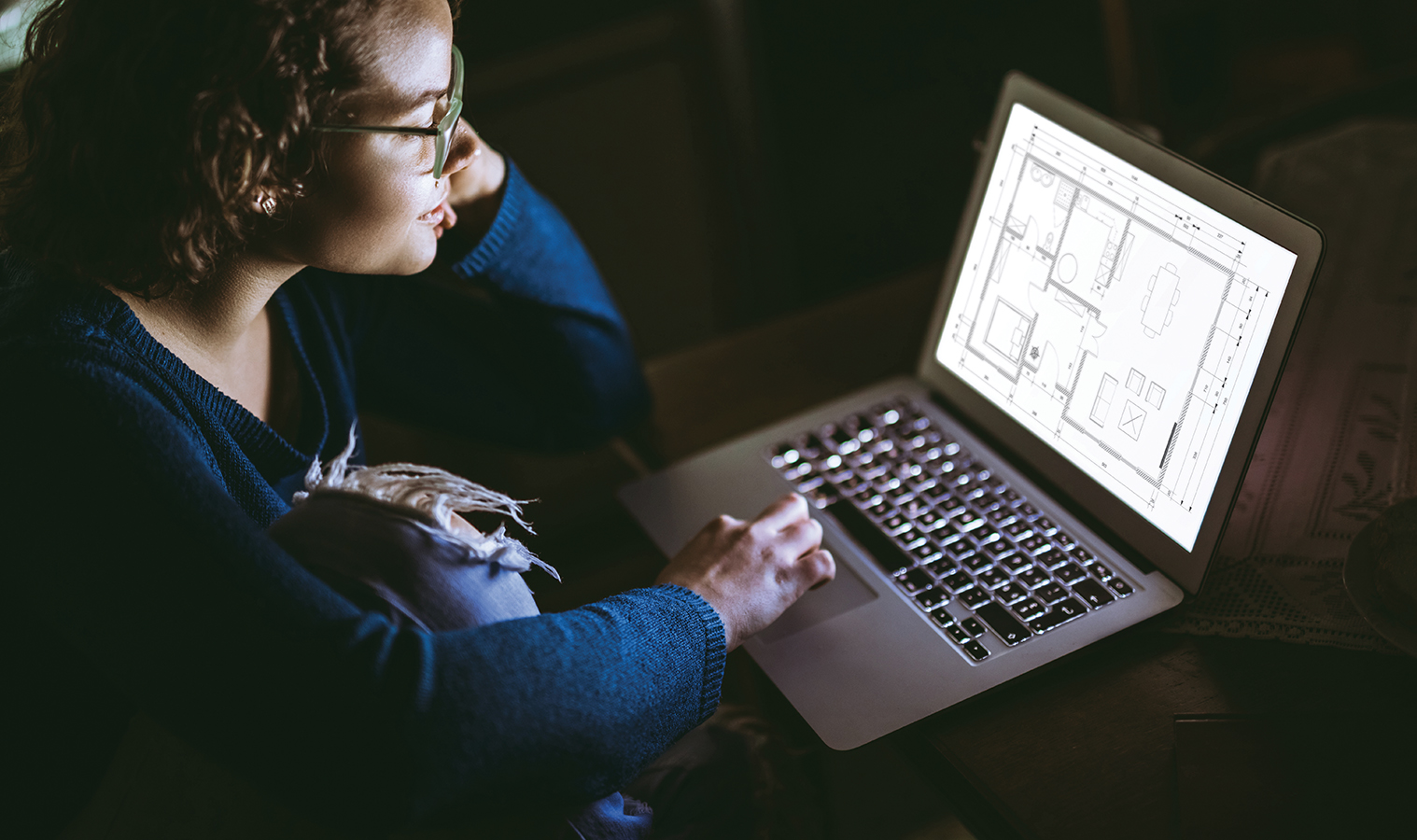 close up on a woman working on a laptop, viewing blueprints of a house. dark room