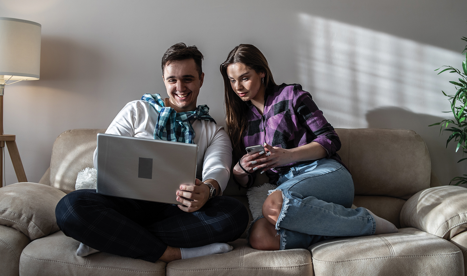 couple sitting comfy on a sofa in a living oom, browsing on a laptop 