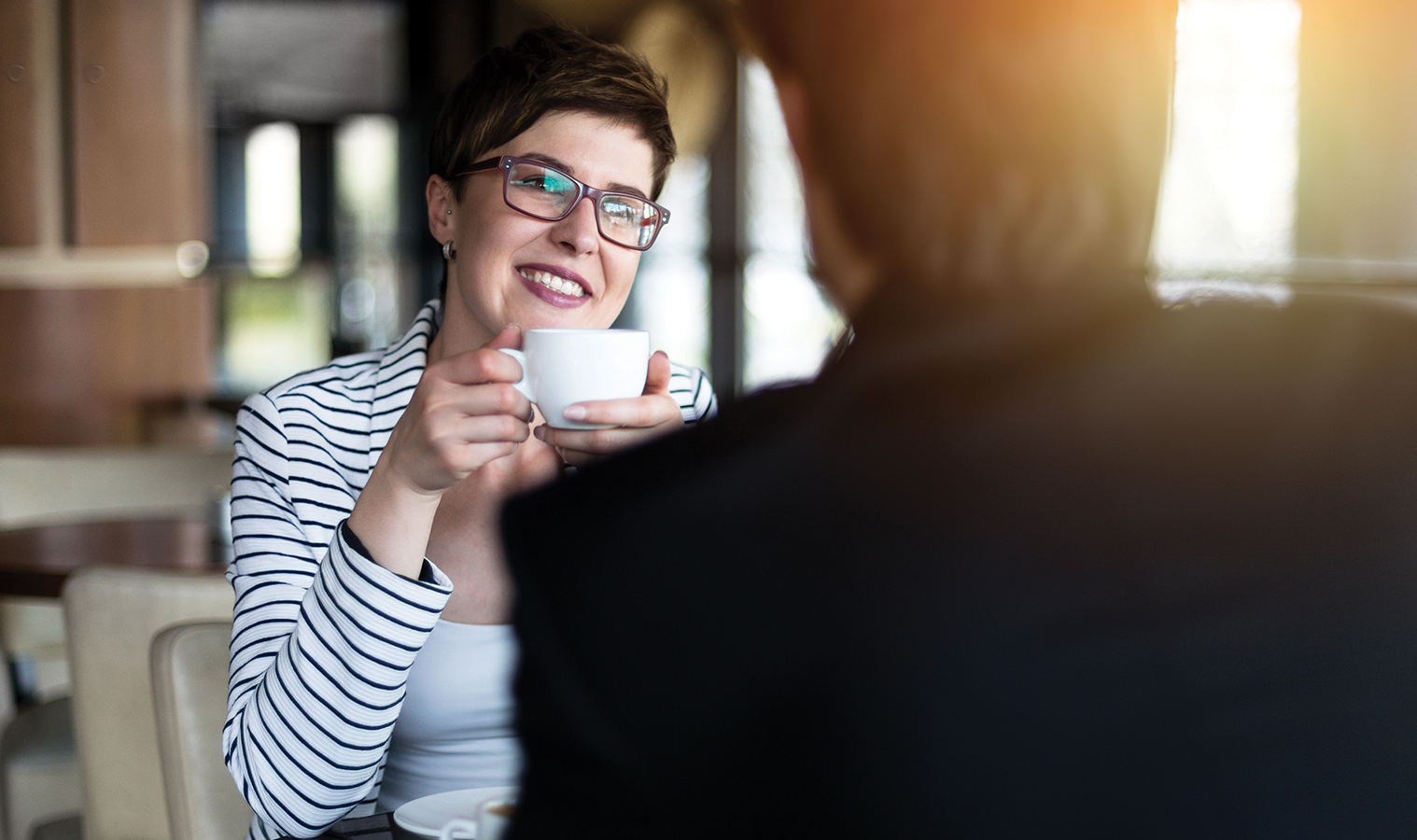 cose up on a couple sitting in a cafe, she's drinking from a small cup, smiling