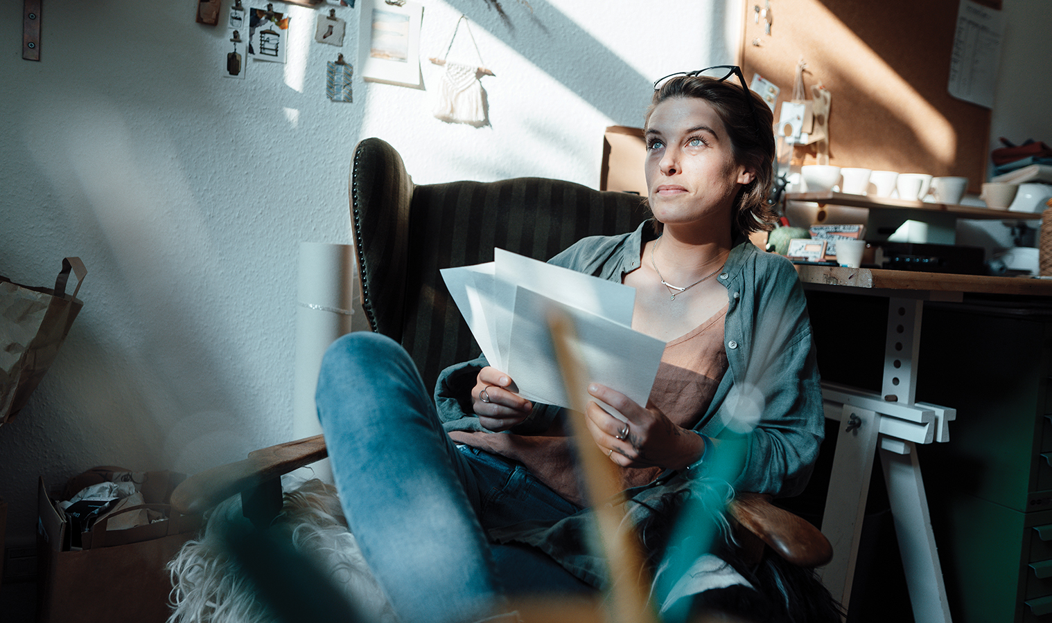 woman sitting comfy in an armchair  holding some pages , looing up to the window